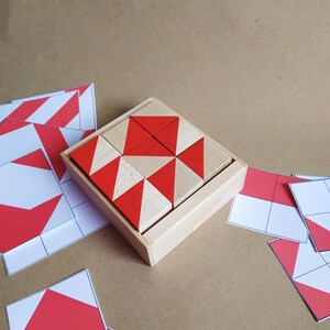 Puede incluir: Una caja de madera con un patr&oacute;n geom&eacute;trico hecho de bloques triangulares rojos y blancos. La caja est&aacute; abierta y los bloques est&aacute;n dispuestos en un patr&oacute;n espec&iacute;fico.