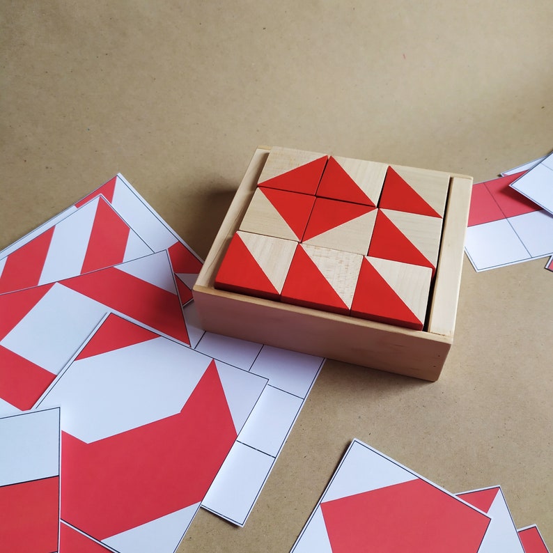 May include: A wooden box with a set of red and white geometric wooden blocks. The blocks are arranged in a pattern and are used for a puzzle or game.
