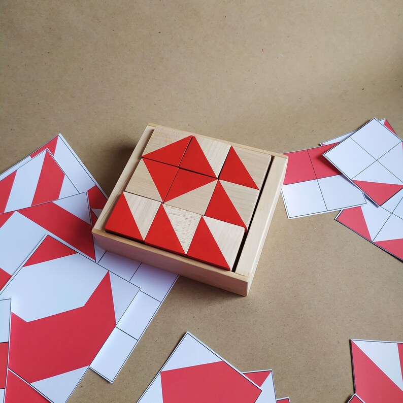 Puede incluir: Una caja de madera con un patr&oacute;n geom&eacute;trico rojo y blanco hecho de bloques triangulares. La caja est&aacute; abierta y los bloques est&aacute;n dispuestos en un patr&oacute;n. Tambi&eacute;n hay varios bloques sueltos con el mismo patr&oacute;n.