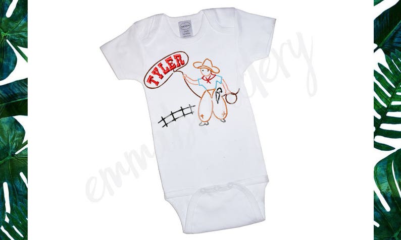 May include: White baby onesie with a red, orange, and brown embroidered design of a cowboy holding a lasso. The onesie has the name "TYLER" embroidered in red on a white speech bubble.