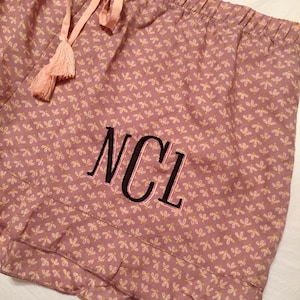 May include: Pink pajama shorts with a white floral pattern and a black embroidered monogram "NCL".