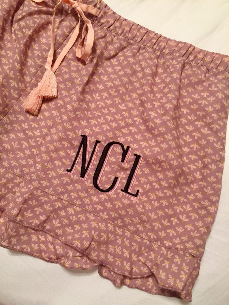 May include: Pink pajama shorts with a white floral pattern and a black embroidered monogram "NCL".