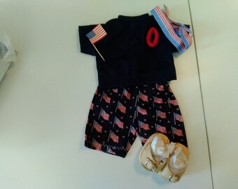 May include: A blue polo shirt with a red number "0" on the front, a pair of blue and white striped shorts with a pattern of American flags, a small American flag on a stick, and a pair of tan sandals.