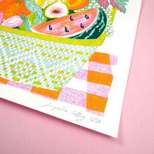 May include: A colorful illustration of a basket overflowing with fruit, including watermelon, figs, and strawberries. The basket is sitting on a pink and orange checkered tablecloth. The image is signed "Jacqueline Tolley 6/50".