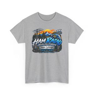 May include: A heather gray t-shirt featuring a colorful graphic print of a mountain landscape, a radio tower, a globe, and a microphone. The text reads HAM RADIO, Adventure Has a Frequency, Your Callsign, DX No Borders Just Friends, and more.