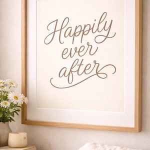 May include: A framed print with the words "Happily ever after" in elegant brown script. The print is set against a cream-colored background, framed in light wood, and displayed on a wall. The scene includes a vase of flowers and a candle.