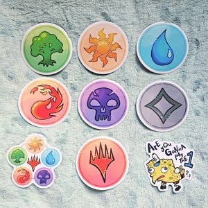 May include: A collection of circular stickers featuring Magic: The Gathering mana symbols in green, orange, blue, red, purple, and grey. One sticker shows all five symbols, another the Planeswalker logo, and one features a cartoon character with the text Are You GONNA pay THE 1??