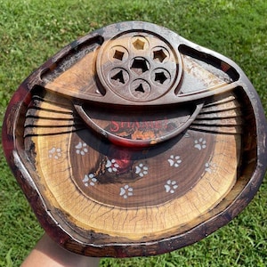 May include: A wooden tray with a red, brown and black finish. The tray has a circular centre section with six cutouts and a smaller, raised circular section with a single cutout. The tray is decorated with white paw prints.