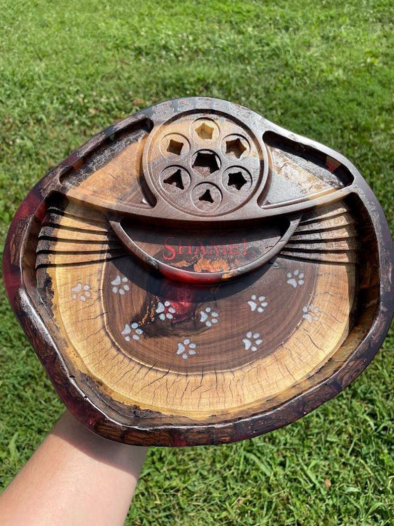 May include: A wooden tray with a red, brown and black finish. The tray has a circular centre section with six cutouts and a smaller, raised circular section with a single cutout. The tray is decorated with white paw prints.