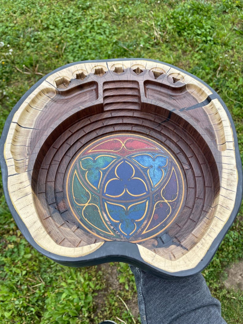 May include: A wooden bowl with a stained glass design in the centre. The bowl is carved to resemble a stadium or arena. The bowl is made of light and dark wood.