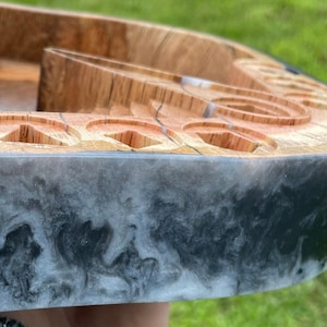 May include: A wooden tray with a black and white epoxy resin border. The tray has multiple circular indentations and a unique design.