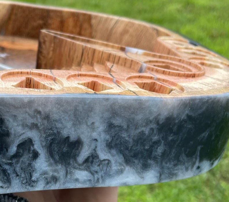 May include: A wooden tray with a black and white epoxy resin border. The tray has multiple circular indentations and a unique design.