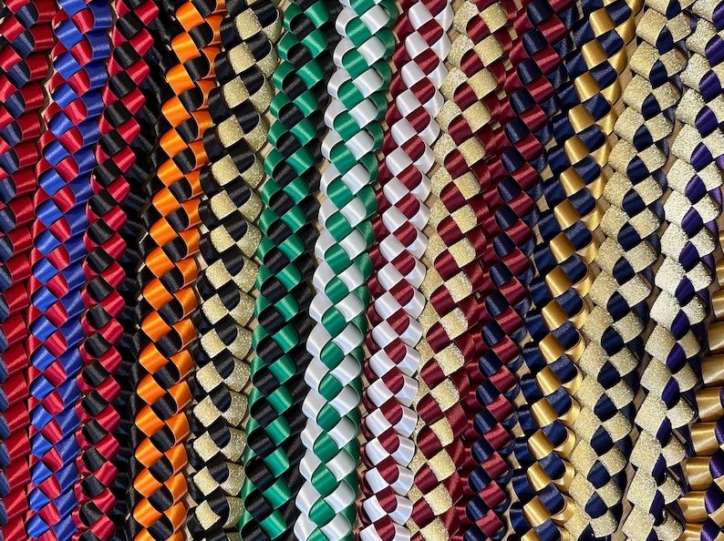 Pu&ograve; includere: Una collezione di collane di nastro intrecciato in vari colori, tra cui rosso, blu, verde, bianco, oro e nero. Le collane sono realizzate con nastro di raso e alcune hanno glitter.