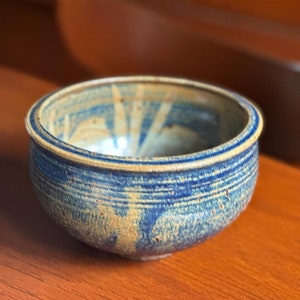 May include: A small, blue and brown ceramic bowl with a speckled glaze. The bowl has a rounded shape and a slightly flared rim.
