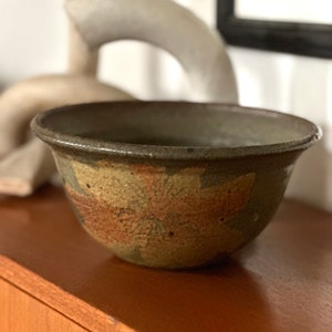 May include: A brown ceramic bowl with a floral design. The bowl has a wide rim and a rounded bottom. The design is in shades of brown, green, and orange.