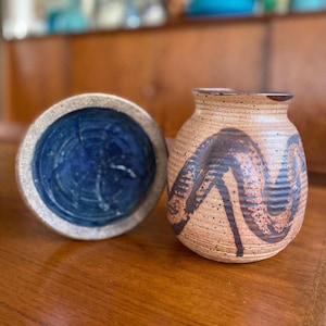 May include: Two ceramic vases with brown and blue glaze. The vase on the left has a blue glaze with a white rim. The vase on the right has a brown glaze with a dark brown swirl design.