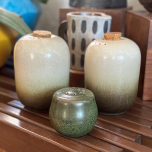 May include: Three ceramic salt and pepper shakers. Two are white with brown speckles and cork tops. One is green with brown speckles.