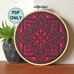 May include: Embroidered hoop art with a geometric design in pink thread on a black background.
