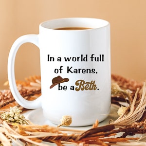May include: White coffee mug with a brown cowboy hat graphic and the text "In a world full of Karens, be a Beth."