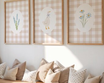 May include: A light wood bookshelf with a bench seat and pillows. The bookshelf is filled with books and there are three framed prints on the wall above the bench. The prints feature a gingham pattern with floral and animal illustrations.