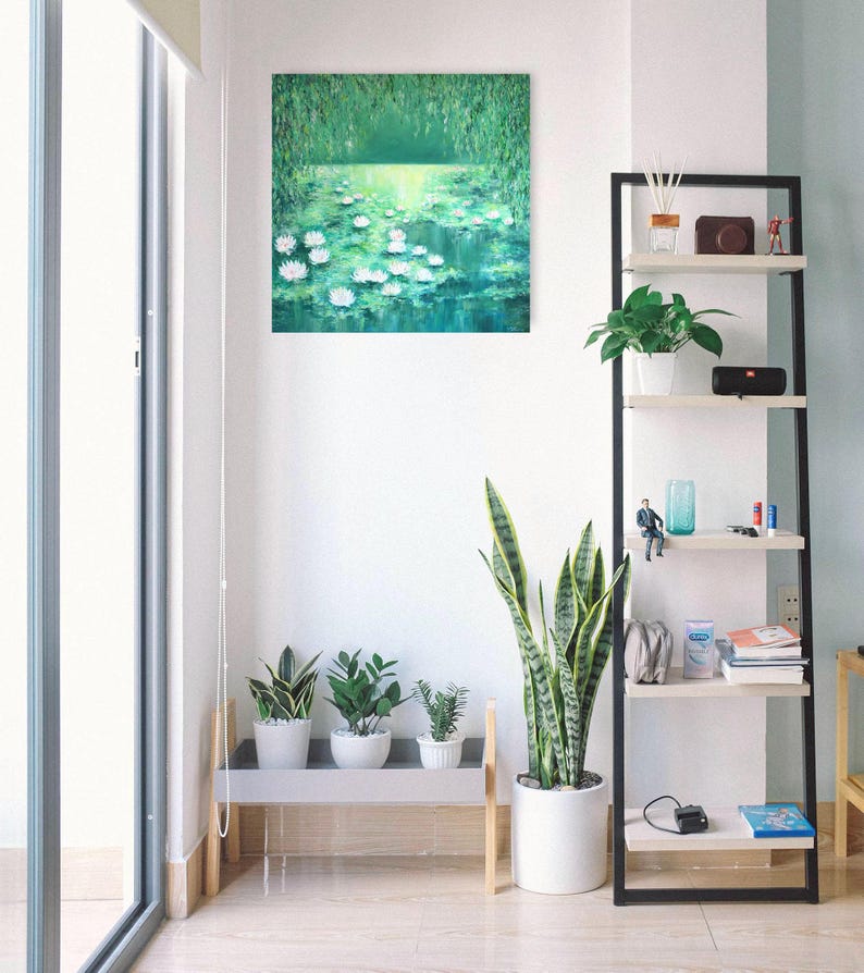 Puede incluir: Una pintura de un estanque con nen&uacute;fares y follaje verde. La pintura est&aacute; colgada en una pared blanca en una habitaci&oacute;n con una estanter&iacute;a y plantas.
