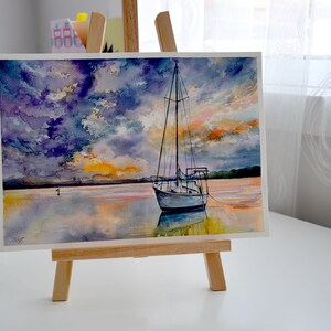 May include: Watercolor painting of a sailboat on a calm body of water with a dramatic sunset sky. The sky is a mix of purple, blue, and orange hues. The sailboat is white with a blue hull and is anchored in the water. The water is a reflective surface with shades of blue, orange, and yellow.