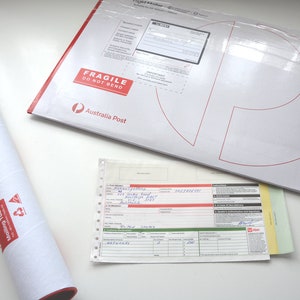 May include: A white mailing tube with red text and a recycling symbol. The tube is rolled up and has a red edge. A white envelope with red text that says "Fragile Do Not Bend" and "Australia Post" is lying flat on a white surface. A white sheet of paper with handwritten text and a red bar code is also on the surface.