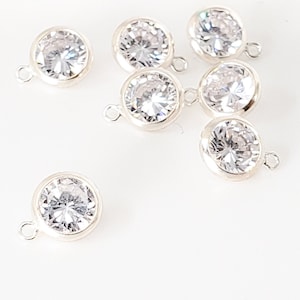 May include: Eight silver-toned round crystal charms with a loop on the side. The crystals are clear and faceted.