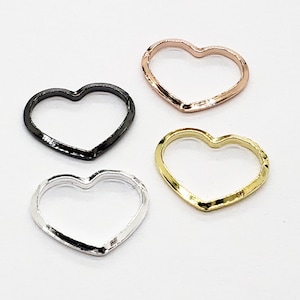 May include: Four heart-shaped metal rings in different colours: silver, gold, black, and rose gold. The rings are open and have a smooth, slightly textured finish.