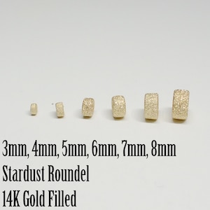 May include: Six gold-filled roundel beads in various sizes, ranging from 3mm to 8mm. The beads have a textured, stardust finish. The text "3mm, 4mm, 5mm, 6mm, 7mm, 8mm Stardust Roundel 14K Gold Filled" is written below the beads.