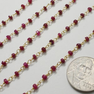 May include: Close-up of several strands of ruby gemstone chain with gold-colored links. The small, faceted rubies are a deep red color. A US quarter coin is included for size reference.