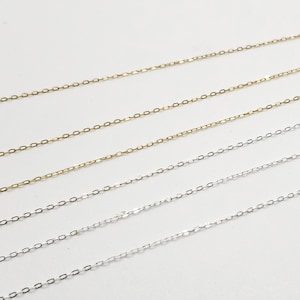 May include: Four chains, two silver and two gold, are laid out on a white surface. The chains are all the same length and have a delicate, oval-link design.