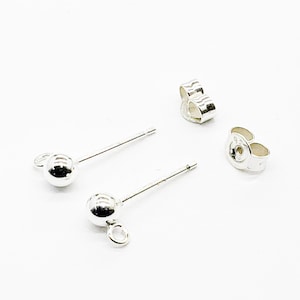 May include: A pair of silver ball stud earrings with matching earring backs. The earrings have a small loop attached to the bottom of the ball. The earrings and backs are on a white background.