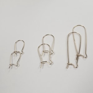 May include: Three gold-toned earring hooks, two are stacked on top of each other, and one is separate. The hooks are made of thin wire and have a simple, rounded shape.
