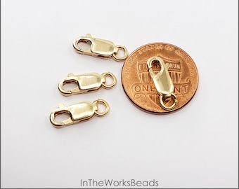 May include: Four 14k gold filled lobster clasps with rings, each measuring 12mm x 4.5mm. The clasps are shown next to a US penny for size comparison.