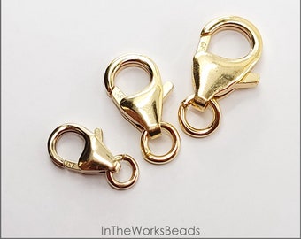 May include: Three gold-filled oval lobster clasps with rings. The clasps are different sizes. The text "14k Gold Filled" is visible at the top of the image. The text "Oval Lobster Clasp with Ring" is visible below the first line of text. The text "3 sizes available, Made in USA" is visible below the second line of text. The text "In The WorksBeads" is visible at the bottom of the image.