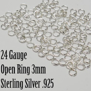 May include: A close-up of a pile of 24 gauge sterling silver open jump rings, each measuring 3mm in diameter. The rings are shiny and silver in color.