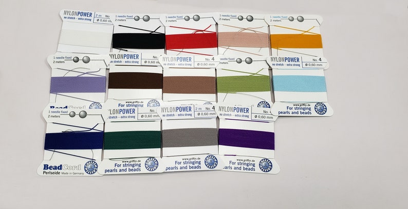 May include: A close-up of 12 spools of nylon thread for stringing beads and pearls. The spools are labeled "Nylon Power" and come in a variety of colors, including black, red, beige, yellow, purple, brown, green, blue, navy, dark green, gray, and purple.