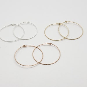 May include: Three pairs of hoop earrings in silver, gold, and rose gold. The earrings are all the same size and have a twisted wire design.