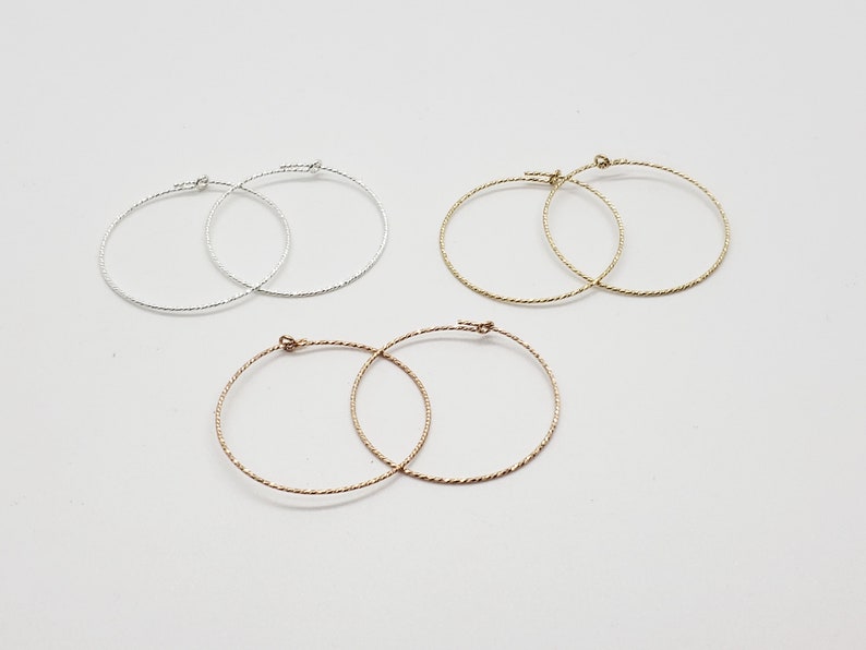 May include: Three pairs of hoop earrings in silver, gold, and rose gold. The earrings are all the same size and have a twisted wire design.