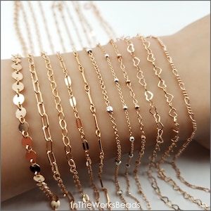 May include: A collection of gold chain bracelets with different styles, including a chain with small round discs, a delicate chain, a chain with small rectangular links, a chain with small round beads, and a chain with heart-shaped links.