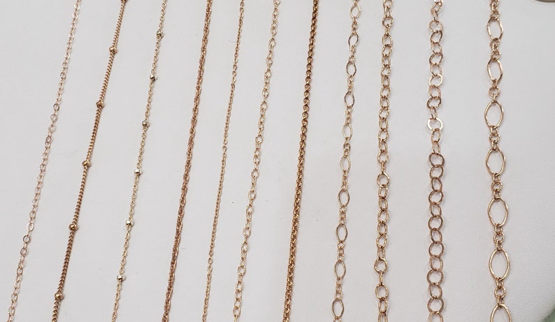 Puede incluir: Una selecci&oacute;n de cadenas de oro de diferentes estilos y longitudes. Las cadenas est&aacute;n dispuestas sobre una superficie blanca.