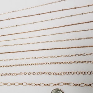 Puede incluir: Una colecci&oacute;n de cadenas de oro de diferentes longitudes y estilos, incluyendo cadenas de cable, curb y caja. Las cadenas est&aacute;n dispuestas en una fila sobre una superficie blanca.