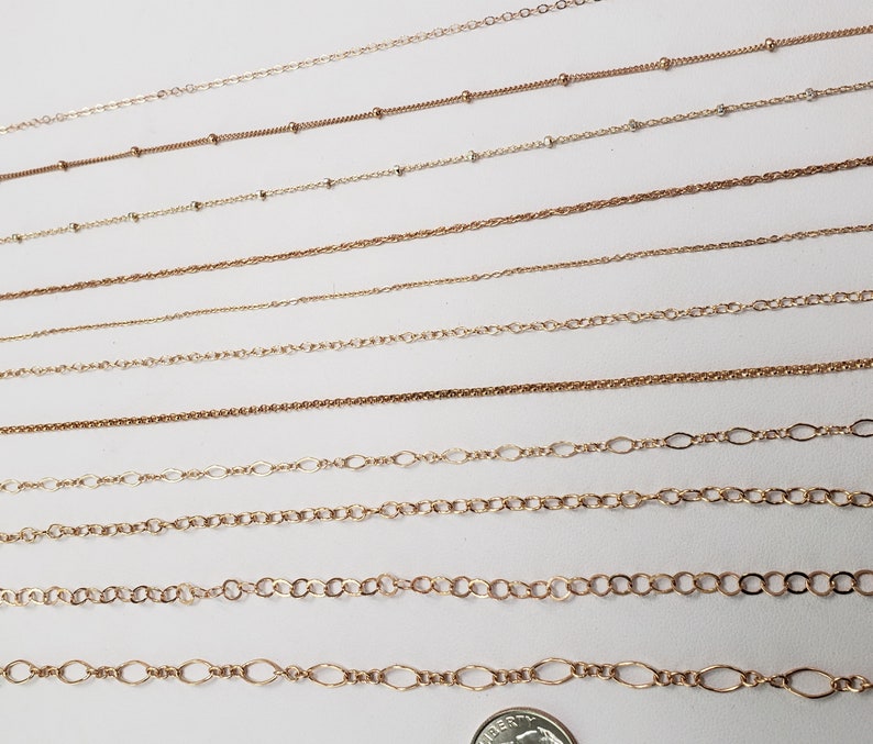 Puede incluir: Una colecci&oacute;n de cadenas de oro de diferentes longitudes y estilos, incluyendo cadenas de cable, curb y caja. Las cadenas est&aacute;n dispuestas en una fila sobre una superficie blanca.