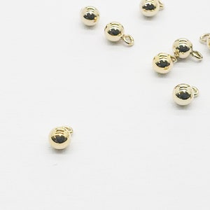 May include: A group of ten gold-colored metal beads with a small loop on each bead.