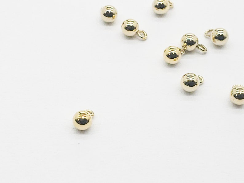 May include: A group of ten gold-colored metal beads with a small loop on each bead.