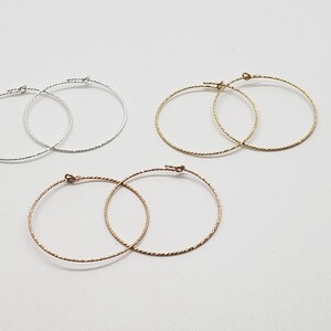 May include: Three pairs of hoop earrings in silver, gold, and rose gold. The earrings are all the same size and have a twisted wire design.