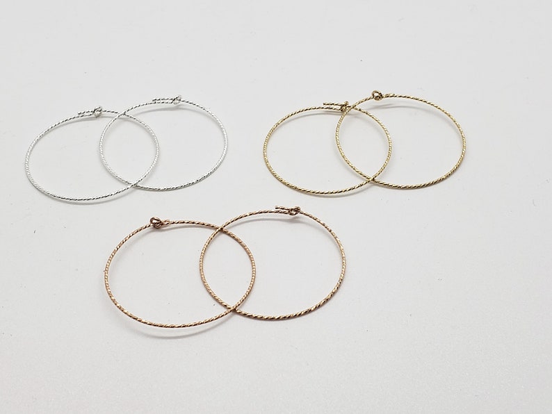 May include: Three pairs of hoop earrings in silver, gold, and rose gold. The earrings are all the same size and have a twisted wire design.
