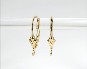 May include: Two gold-colored leverback earrings. Each earring features a decorative, stylized design at the bottom and a curved lever. The earrings are displayed against a white background.
