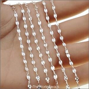 May include: Five strands of silver chain with a faceted oval link design. The chain is shown on a hand, with the ends of the chain hanging down.